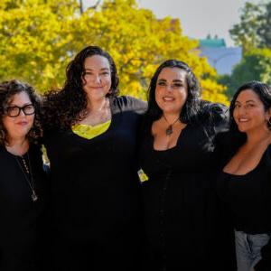 Jessica J. Chairez '13, Jack Contreras '22, Tricia Morgan '08, and Crystal Rodriguez '23 wear all black and stand side by side on a balcony overlooking Pitzer's campus.
